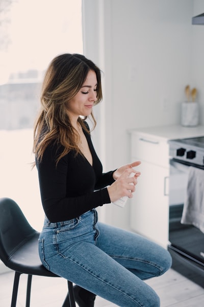 Dressed in a black long sleeved shirt and a blue denim jeans woman sitting on a white table
